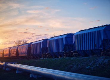 Train with wagons loaded with grain moves at sunset along the pipeline